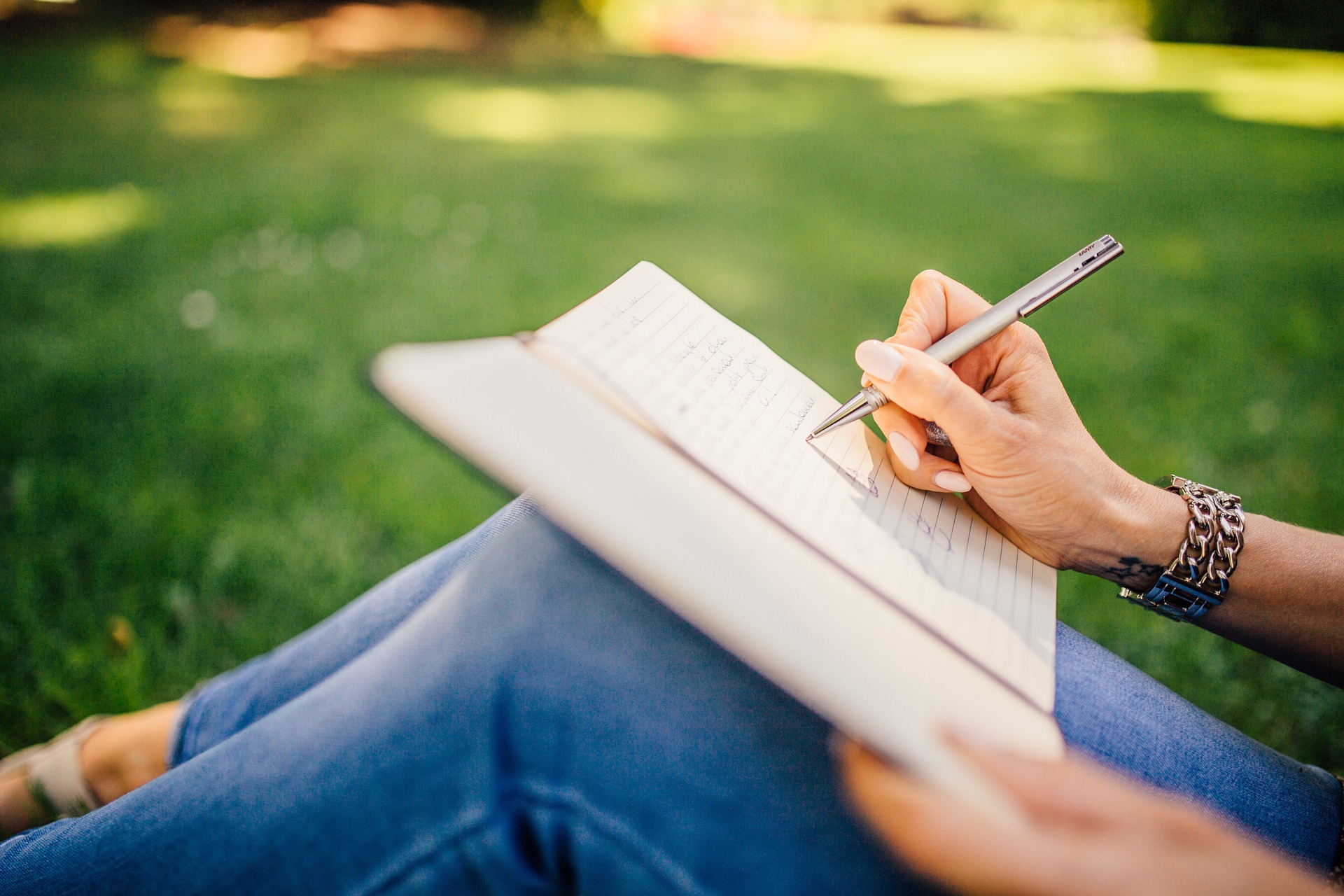 Person journaling while sitting in the grass. Stock photo.